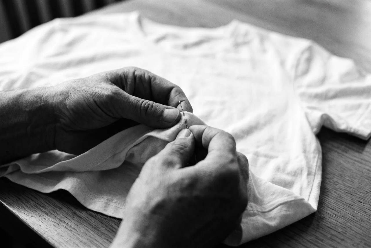 Stimmungsbild: Hände arbeiten mit einer Nadel am Shirtsaum